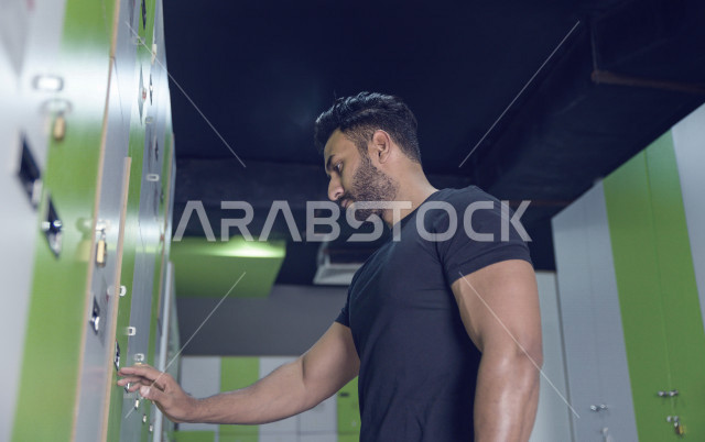 شاب عربي خليجي سعودي يفتح الخزانة و يستعد للتدريب ، رجل يضع أغراضه الخاصة في الخزانة في النادي الرياضي