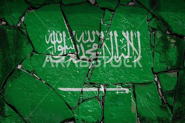 علم المملكة العربية السعودية مرسوم بألوان زاهية على جدار حجري قديم. راية العلم على خلفية جدار متصدع. علم المملكة العربية السعودية مرسوم بألوان زاهية على جدار حجري قديم. راية العلم على خلفية جدار متصدع.