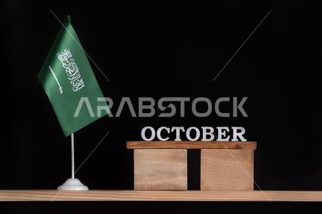 تقويم خشبي لشهر أكتوبر عليه علم المملكة العربية السعودية على خلفية سوداء. تواريخ المملكة العربية السعودية في شهر أكتوبر.
