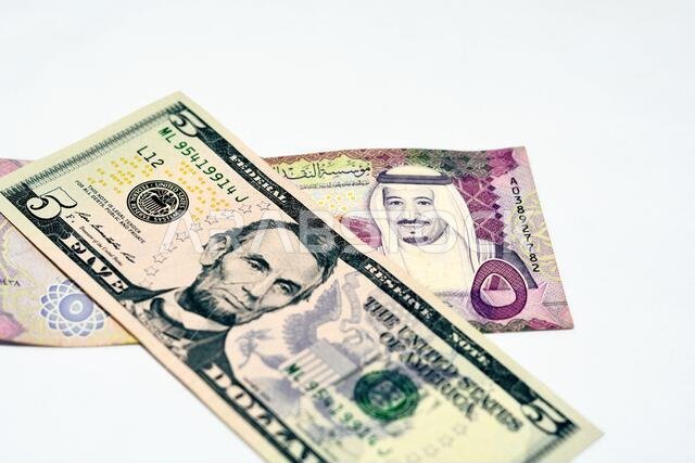 التركيز الانتقائي على ورقة نقدية أمريكية من فئة خمسة دولارات وريال سعودي من فئة خمسة ريالات سعودية، والعملة السعودية والدولار الأمريكي