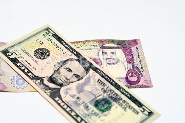 التركيز الانتقائي على ورقة نقدية أمريكية من فئة خمسة دولارات وريال سعودي من فئة خمسة ريالات سعودية، والعملة السعودية والدولار الأمريكي
