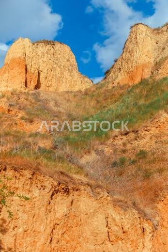 منظر طبيعي لجرف رأس الطين. عشب أخضر، ومروج تنمو على سفوح جبال الطين مقابل السماء الزرقاء. تلال جبلية وسفوح رأس الطين