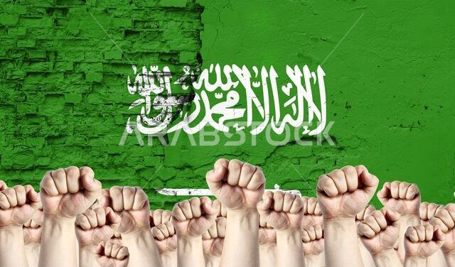 Raised fists of men against the background of the flag of Saudi Arabia painted on the wall, the concept of popular unity and the opinion of the majori Raised fists of men against the background of the flag of Saudi Arabia painted on the wall, the concept of popular unity and the opinion of the majori