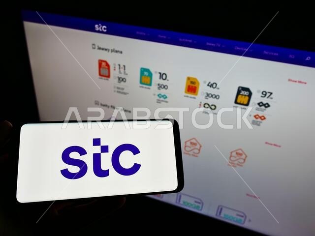 Person holding cellphone with logo of Arabian carrier Saudi Telecom Company (STC) on screen in front of company website. Focus on phone display.
