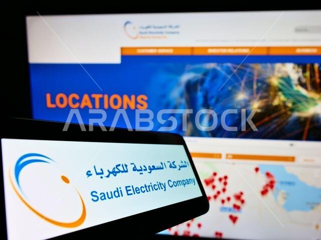 هاتف ذكي يعرض شعار شركة الكهرباء السعودية على شاشته أمام موقع إلكتروني. التركيز على منتصف يمين شاشة الهاتف.