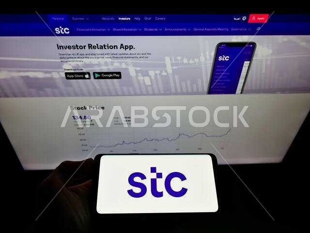 Person holding smartphone with logo of Arabian carrier Saudi Telecom Company (STC) on screen in front of website. Focus on phone display.