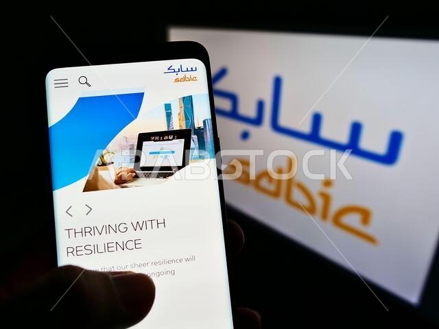 شخص يحمل هاتفًا محمولًا يعرض موقع شركة سابك (الشركة السعودية للصناعات الأساسية) على الشاشة مع شعارها. التركيز على منتصف شاشة الهاتف. شخص يحمل هاتفًا محمولًا يعرض موقع شركة سابك (الشركة السعودية للصناعات الأساسية) على الشاشة مع شعارها. التركيز على منتصف شاشة الهاتف.