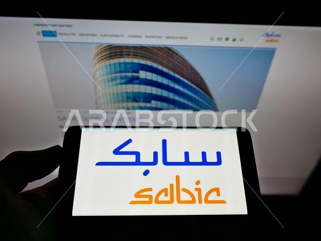 شخص يحمل هاتفًا محمولًا عليه شعار شركة سابك (الشركة السعودية للصناعات الأساسية) على الشاشة أمام صفحة الويب. التركيز على شاشة الهاتف.