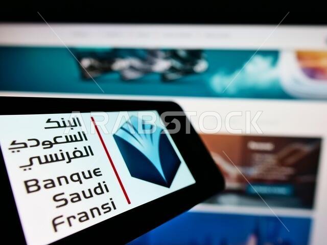 هاتف محمول يحمل شعار بنك السعودي الفرنسي (BSF) على شاشته أمام موقع إلكتروني تجاري. التركيز على منتصف شاشة الهاتف.