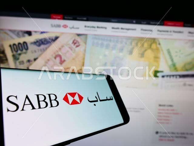 هاتف ذكي يعرض شعار شركة التمويل السعودية البريطانية (ساب) على الشاشة أمام صفحة الويب. التركيز على منتصف يسار شاشة الهاتف. هاتف ذكي يعرض شعار شركة التمويل السعودية البريطانية (ساب) على الشاشة أمام صفحة الويب. التركيز على منتصف يسار شاشة الهاتف.