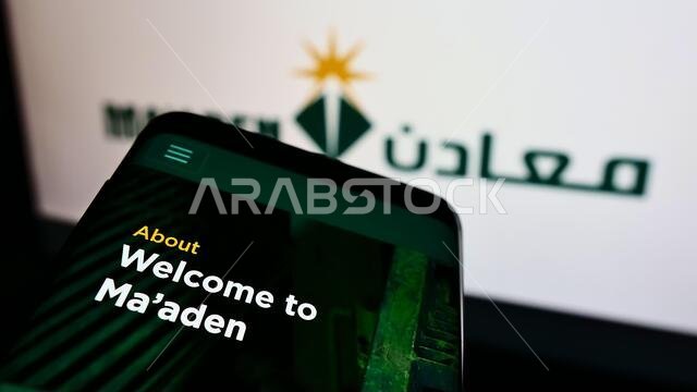 هاتف محمول يعرض موقع شركة التعدين السعودية (معادن) على الشاشة أمام شعار الشركة. التركيز على أعلى يسار شاشة الهاتف.