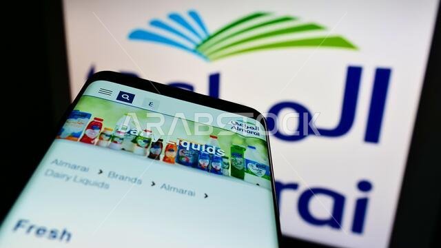 هاتف محمول يعرض موقع شركة المراعي السعودية للألبان على الشاشة أمام شعار الشركة. ركّز على الزاوية العلوية اليسرى من شاشة الهاتف.