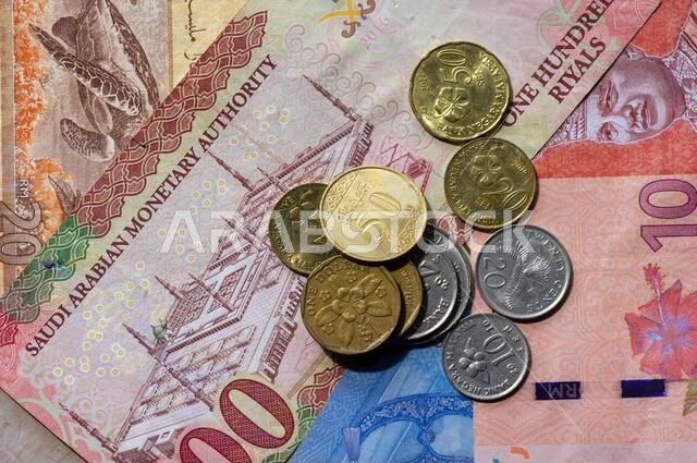 صورة علوية للنقود، مع أوراق نقدية من الرينغيت الماليزي والدولار السنغافوري والريال السعودي كخلفية. (قطاع الأعمال والمالية والاقتصاد والاستثمار)