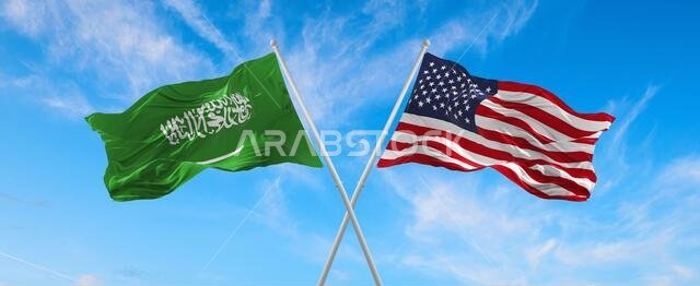 flags of USA and Saudi Arabia waving in the wind on flagpoles against the sky with clouds on sunny day. Symbolizing relationship, dialog between two c