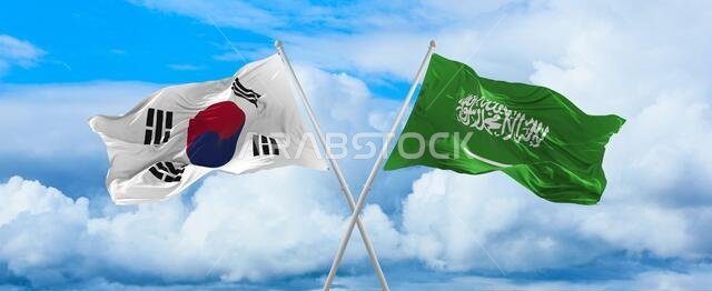 أعلام كوريا الجنوبية والمملكة العربية السعودية ترفرف في مهب الريح على أعمدة الأعلام في سماء ملبدة بالغيوم في يوم مشمس. ترمز إلى العلاقة والحوار بين البلدين.