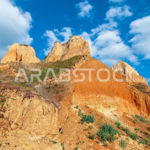 منظر طبيعي لجرف رأس طيني. تلال الجبل ومنحدرات الرأس مغطاة جزئيًا بالعشب والنباتات. عشب أخضر، ومروج تنمو على المنحدرات