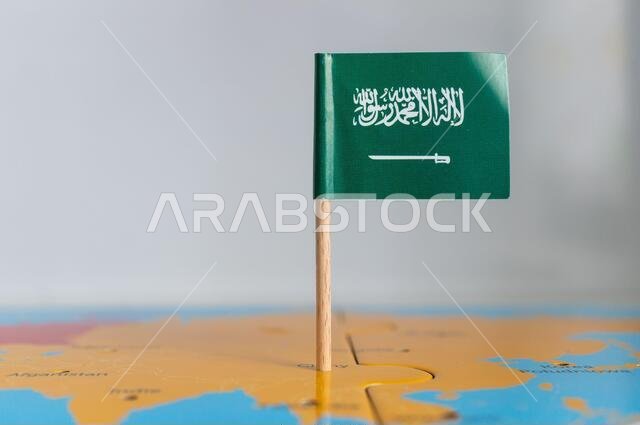 علم صغير للمملكة العربية السعودية مثبت على عصا خشبية فوق الكرة الأرضية