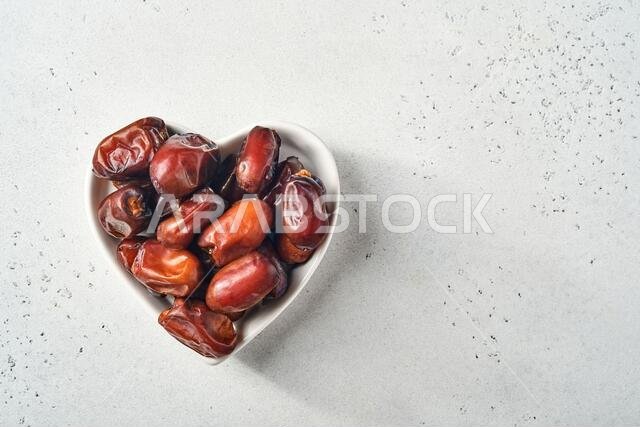 Dried sliced date fruit in a heart-shaped ceramic plate on white background with copy space. Snack vegan sugarfree food.
