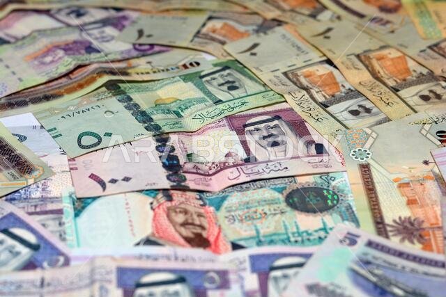 مجموعة من خلفيات العملات السعودية، ومجموعة مختلفة من الريالات السعودية من فئات 100 و50 و20 و10 و5 و1 ريال، مع التركيز بشكل انتقائي على العملات السعودية.