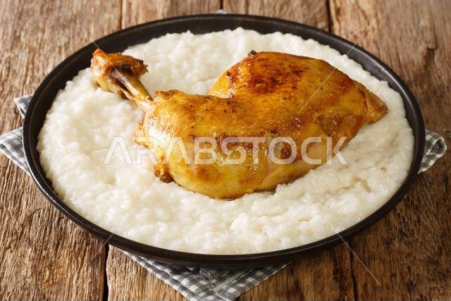أرز لذيذ مطبوخ في مرق مع حليب وزبدة، وقطع دجاج مقرّبة على طبق على الطاولة. أفقي