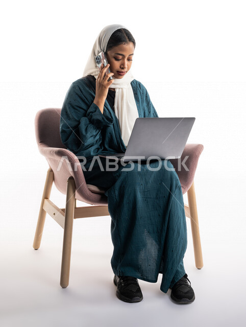 بورتريه لإمرأة عربية خليجية سعودية تستخدم جهاز الحاسوب المحمول وتقوم باجراء مكالمة من خلال الهاتف المحمول، مكالمة هاتفية، العمل عن بعدمكالمة خاصة بالعمل، اتصال وتواصل اجتماعي، متابعة اهداف ومهام العمل، خلفية بيضاء