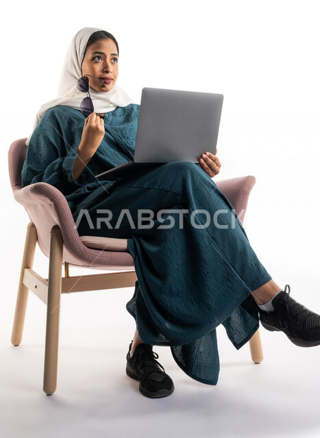 Portrait of a Saudi Arabian Gulf woman using a laptop computer and holding sunglasses in her hand, working remotely, completing work tasks, sunglasses, facial gestures indicating confusion and thinking, white background