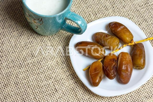 Top view of Algerian dates on a white plate with a mug of milk, Ramadan concept, space for text