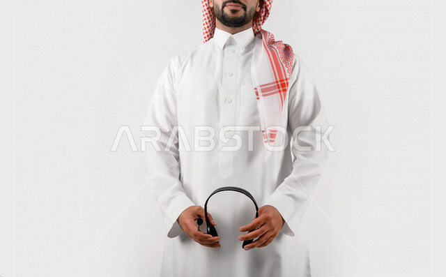 بورتريه بصورة مقربة لموظف عربي خليجي سعودي يحمل بيده سماعة الرأس الصوتية ، العمل في مجال خدمة العملاء ، استعلامات و استفسارات ، الاجابه على اسئلة العملاء ، سماعة الإتصال ، الدعم الفني ، مهن و وظائف ، خلفية بيضاء