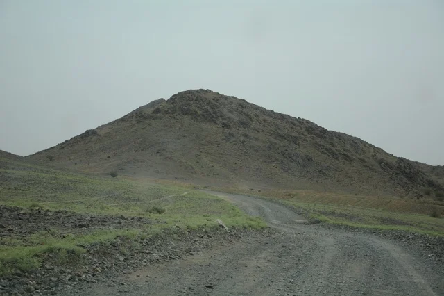 طريق ترابي ممتد نحو جبل صحراوي أخضر في السعودية