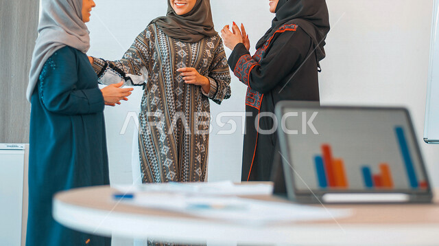 A group of Saudi Gulf businesswomen in a meeting inside a Saudi company, analysis of sales data and chart of economic growth, business and financial strategy, follow-up of the stock market through the tablet, background of the chart
