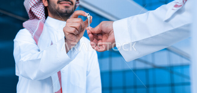 صورة مقربة لرجل عربي خليجي سعودي يستلم مفتاح المشروع الخاص به ، وكيل عقارات يعطي المفاتيح لصاحب البناء ، مهندس ينهي مشروع البناء ، شراء بيت جديد ، عقار جديد ، إستثمار عقاري ، مفهوم الأعمال التجارية العقارية