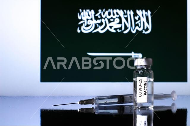 قارورة تحتوي على لقاح كوفيد-19 وحقنة. علم المملكة العربية السعودية في الخلفية
