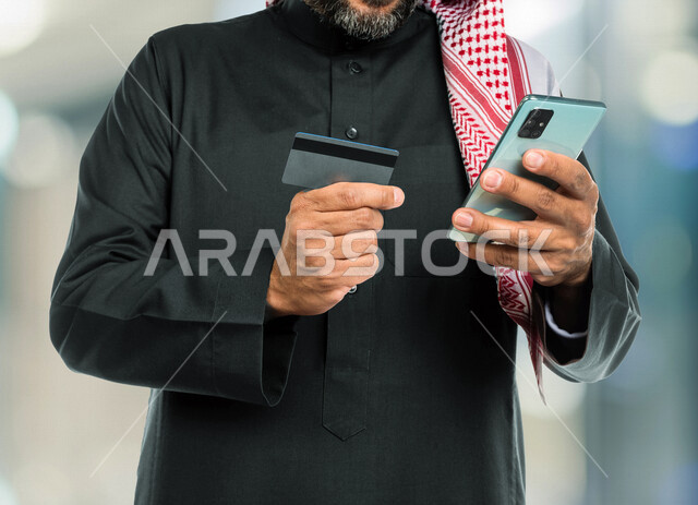 صوة مقربة لرجل عربي سعودي خليجي يستخدم الهاتف المحمول، استخدام بطاقة الصراف للدفع الإلكتروني، التسوق عبر الإنترنت، التجاره الإلكترونيه، الإستثمار المالي، طلبات الأونلاين، الدفع عن طريق بطاقة الإئتمان، الشراء عبر برامج وتطبيقات الجوال