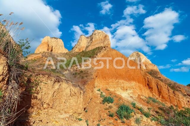 منظر طبيعي لجرف رأس الطين. عشب أخضر، ومروج تنمو على سفوح جبال الطين مقابل السماء الزرقاء. تلال جبلية وسفوح رأس الطين تغطيها السماء.