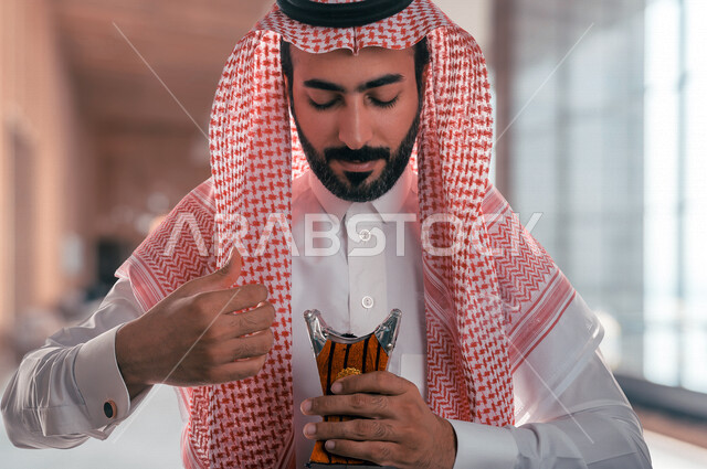رجل عربي خليجي سعودي يحمل بيده المبخرة، حامل البخور، استخدام خشب العود في المناسبات الاجتماعية والمناسبات الدينية، اصالة العادات والتقاليد في المملكة العربية السعودية ، التطيب والتعطر