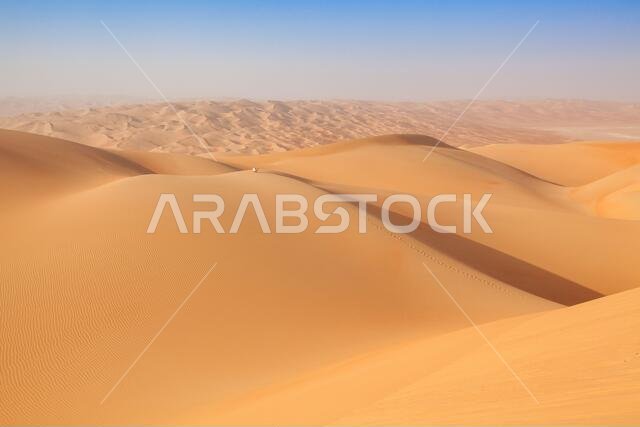 Man in traditional omani outfit sitting over a sand dune in the arabian desert