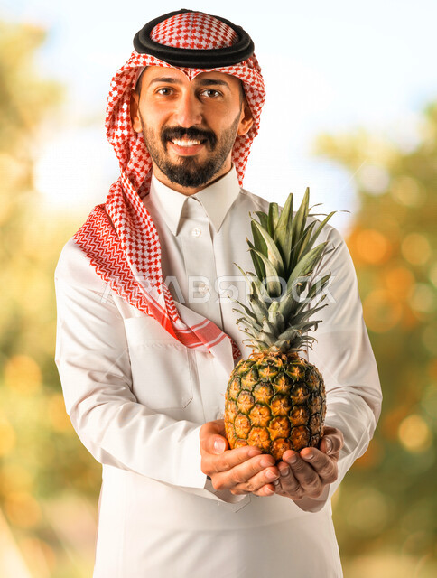 بورتريه لرجل عربي خليجي سعودي يحمل بيده فاكهة الأناناس، فواكه صحية، تناول وجبة طعام صحيه خفيفه، وجبات الدايت، الصحة والرشاقة، إيماءات وجه مبتسمة، خلفية الطبيعة