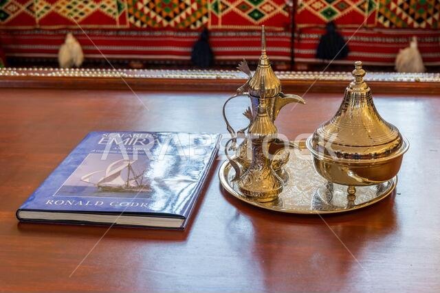 Copper antique Arabian tea pot and a travel guide book  with background of Arabian traditional sofa