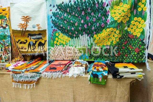 وشاح وسجادة عربية تقليدية بنقوش ملونة معروضة للبيع في قرية التراث الشعبي في أبو ظبي، الإمارات العربية المتحدة.
