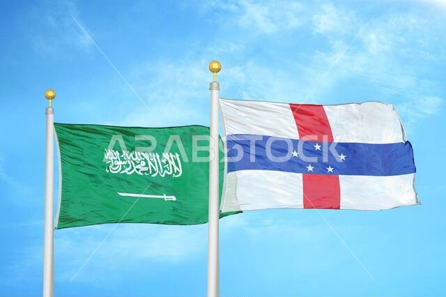 علمان للمملكة العربية السعودية وجزر الأنتيل الهولندية على ساريتين وسماء زرقاء ملبدة بالغيوم