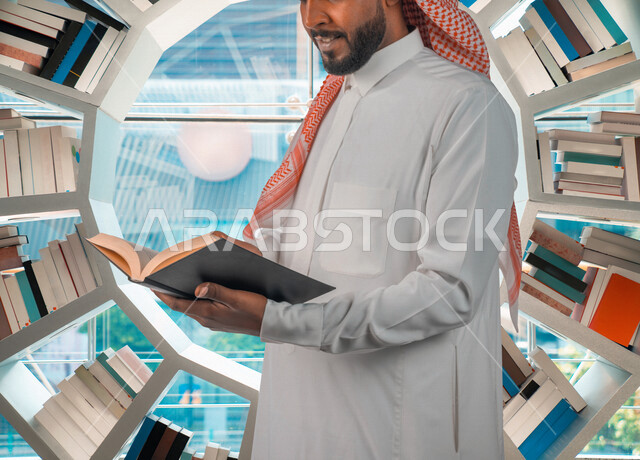 رجل عربي سعودي خليجي في المكتبة، قراءة كتاب داخل المكتبة, استعارة كتاب مناسب، الدراسه في مكتبة الجامعه, اثراء التعليم الجامعي، البحث العلمي، مفهوم العلم والتعلم