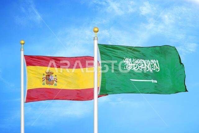 Spain and Saudi Arabia two flags on flagpoles and blue cloudy sky