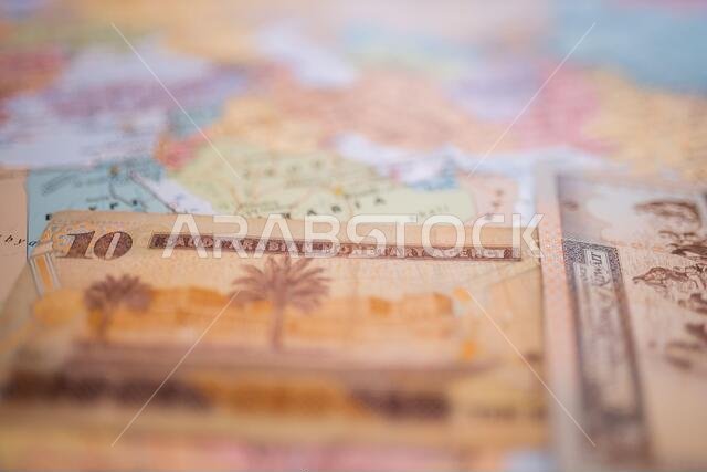 Ten riyals bill and a Quarter Dinar bill below Saudi Arabia on a colorful map