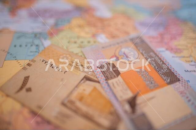 Ten riyals bill and a Quarter Dinar bill above Saudi Arabia on a colorful map