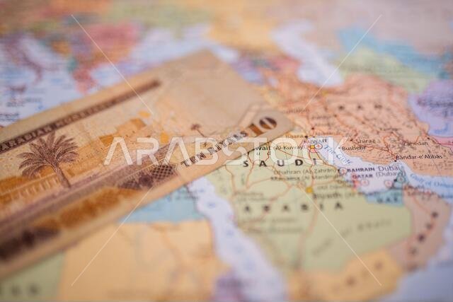 ورقة نقدية من فئة عشرة ريالات فوق المملكة العربية السعودية على خريطة ملونة وغير واضحة لغرب آسيا