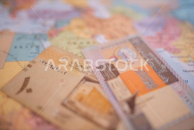Ten riyals bill and a Quarter Dinar bill above Saudi Arabia on a colorful map