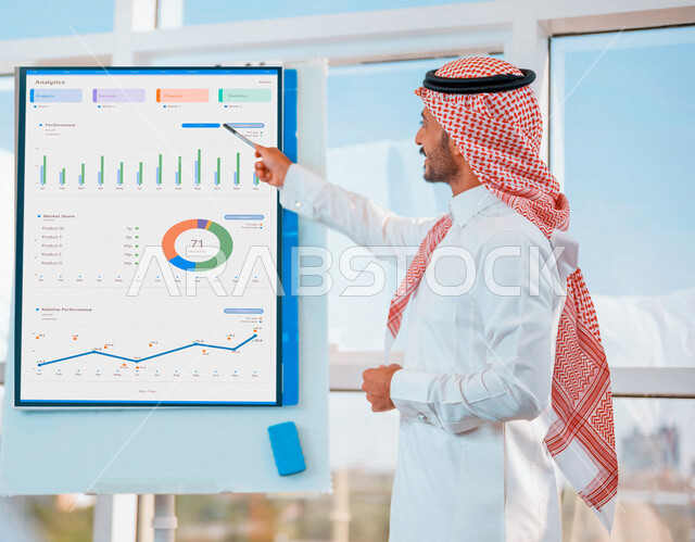 رجل أعمال عربي خليجي سعودي في مقر عمله ، يقوم بشرح الرسومات البيانية لتطوير المشاريع، دراسة وتحليل المشاريع الجديدة، تقييم العمل الشراكي، الشراكة والتعاون، اجتماعات عمل، ورش عمل وتدريب