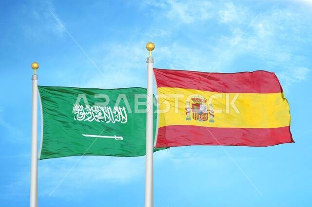 Saudi Arabia and Spain two flags on flagpoles and blue cloudy sky