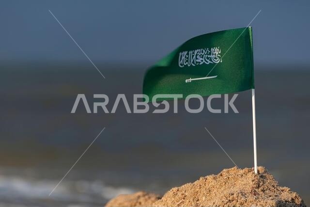 Flag of Saudi Arabia on sandy shore. National flag of Saudi Arabia on sea background. Green flag with sword