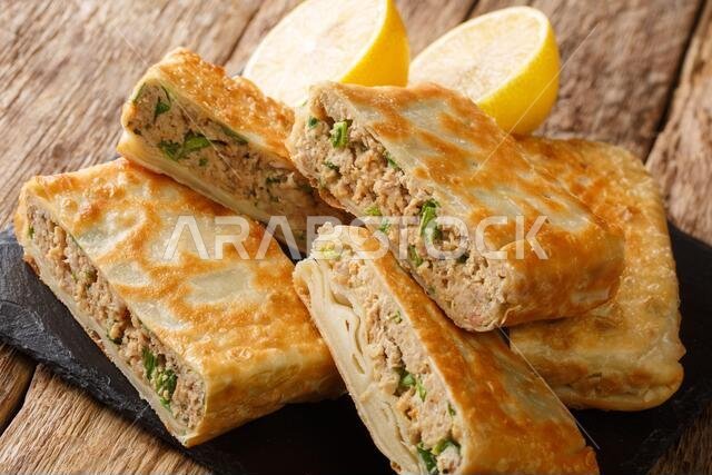 المطباق هو خبز عربي محشو بالبيض واللحم المتبل، ويظهر في صورة مقربة على لوح خشبي موضوع على الطاولة.